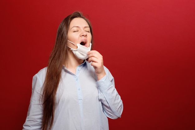 Retrato de mujer joven en la pared roja en máscara médica protectora, estornuda