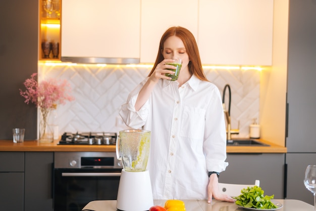 Retrato de mujer joven pelirroja atractiva beber jugo de batido de desintoxicación de vegetales saludables en