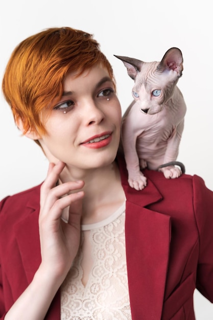 Retrato de mujer joven pelirroja hipster con pelo corto vestido con chaqueta roja y gato sphynx juguetón