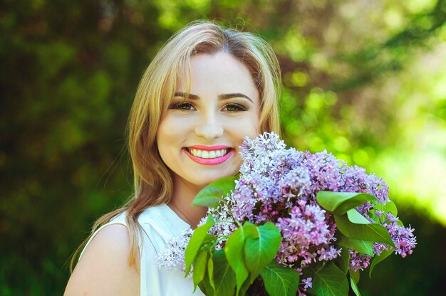 Retrato de mujer joven pelirroja en el jardín de primavera. pecas florecientes flores de color púrpura. Ramo de lilas