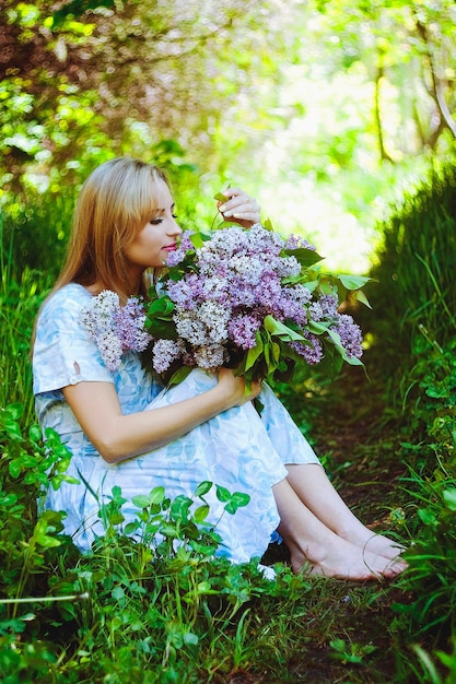 Retrato de mujer joven pelirroja en el jardín de primavera. pecas florecientes flores de color púrpura. Ramo de lilas