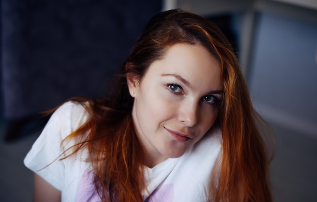 Retrato de mujer joven pelirroja con piel suave perfecta. Rostro de niña hermosa, primer plano. Modelo femenino en camiseta blanca mira a cámara y sonríe.