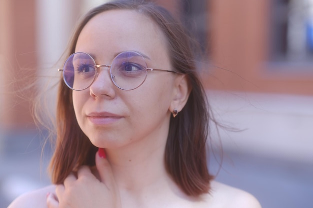 Retrato de mujer joven con pelo corto en gafas mirando hacia otro lado de pie en la calle de la ciudad en un clima cálido y ventoso