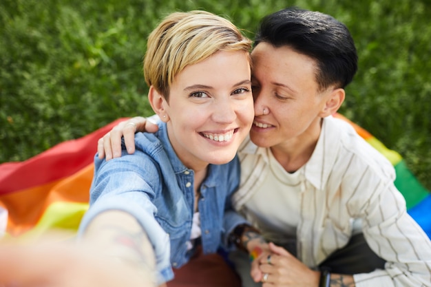 Retrato de mujer joven con pelo rubio corto sonriendo mientras toma selfie retrato con su novia al aire libre