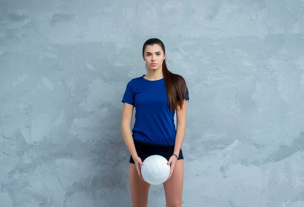 Foto retrato de una mujer joven con una pelota de voleibol de pie contra la pared