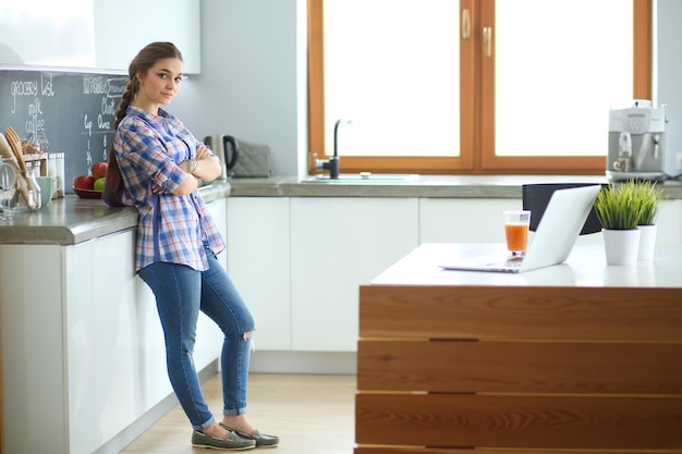 Retrato de mujer joven de pie con los brazos cruzados contra el fondo de la cocina