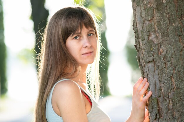 Retrato de mujer joven de pie cerca de un árbol