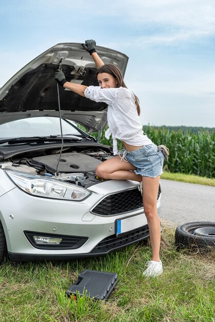 Foto retrato de una mujer joven de pie cerca de un coche roto durante un viaje de verano necesitamos ayuda servicio de automóviles