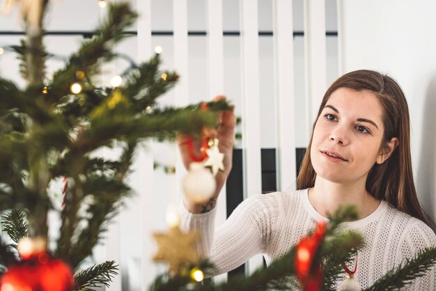 Foto retrato de una mujer joven de pie contra el árbol de navidad