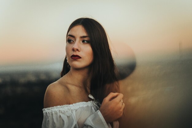 Foto retrato de una mujer joven de pie contra el cielo durante la puesta de sol