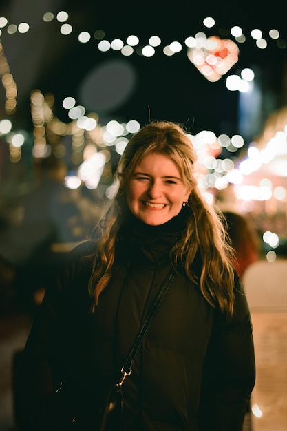 Retrato de una mujer joven de pie contra luces de cuerda iluminadas por la noche