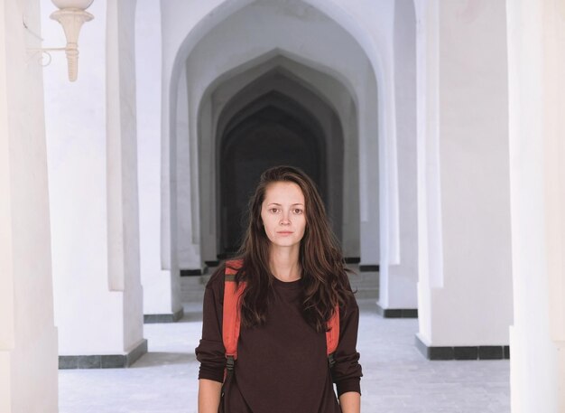 Foto retrato de una mujer joven de pie en un corredor de arcos árabes blancos en la mezquita de kalyan bukhara uzbekistan