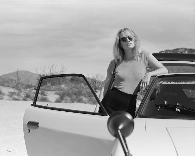 Foto retrato de una mujer joven de pie junto al coche contra el cielo