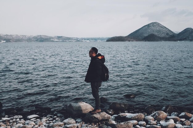 Retrato de una mujer joven de pie en una roca junto al mar contra el cielo