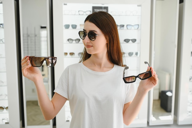 Retrato de una mujer joven de pie en la tienda y probando gafas de sol cerca de un espejo