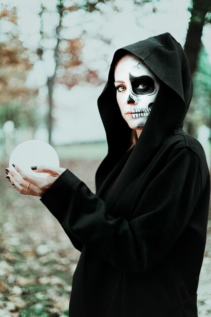 Foto retrato de una mujer joven con pintura facial sosteniendo una bola de cristal en el bosque