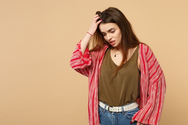 Retrato de mujer joven preocupada en ropa casual mirando hacia abajo, poniendo la mano en la cabeza aislada sobre fondo beige pastel en estudio. Personas sinceras emociones, concepto de estilo de vida. Simulacros de espacio de copia.