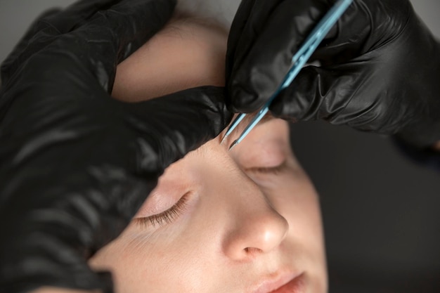 Retrato de mujer joven en el procedimiento de corrección de cejas Cosmetólogo en guantes negros arranca las cejas con pinzas