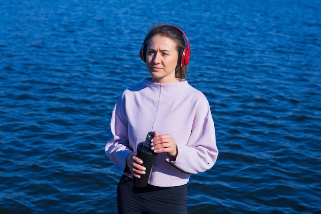 Retrato de una mujer joven que bebe agua durante un descanso al aire libreMúsica durante el entrenamiento con auriculares rojos