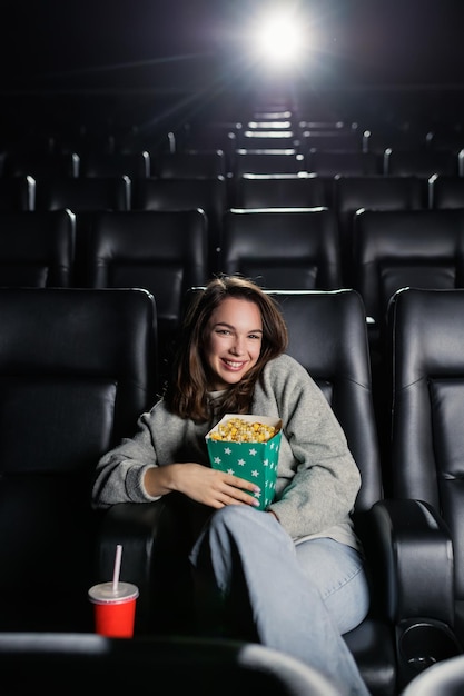 Foto retrato de una mujer joven que mira a la cámara con una sonrisa mientras está sentada en un cine una mujer en el estreno de una película largamente esperada