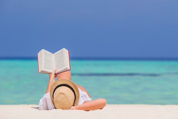 Retrato de una mujer joven que se relaja en la playa, leyendo un libro