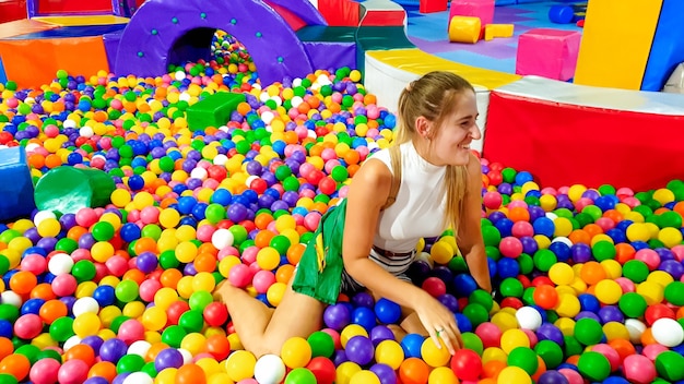 Retrato de mujer joven riendo cayendo en la piscina con un montón de bolas de plástico de colores en los niños palyground en el centro comercial