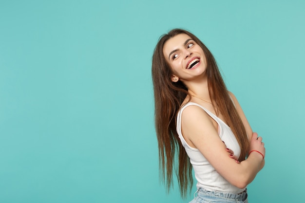 Retrato de mujer joven riendo en ropa casual ligera mirando a un lado cogidos de la mano cruzados aislados sobre fondo de pared azul turquesa. Concepto de estilo de vida de emociones sinceras de personas. Simulacros de espacio de copia.