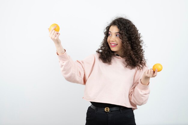 Retrato de mujer joven rizada en suéter rosa con naranjas.