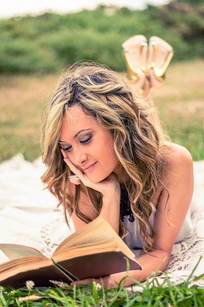 Retrato de mujer joven romántica leyendo un libro acostado sobre la hierba. Relajarse el concepto de tiempo al aire libre.