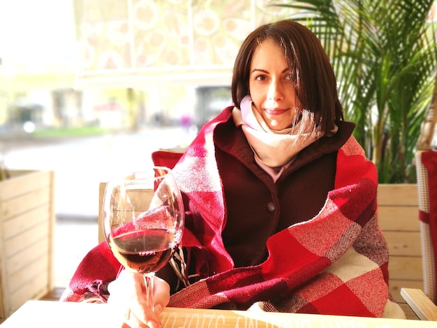 Foto retrato de una mujer joven con ropa cálida tomando vino mientras está sentada en casa