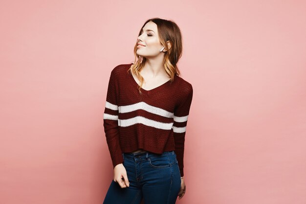 Retrato de una mujer joven con ropa casual con auriculares inalámbricos, sobre fondo rosa