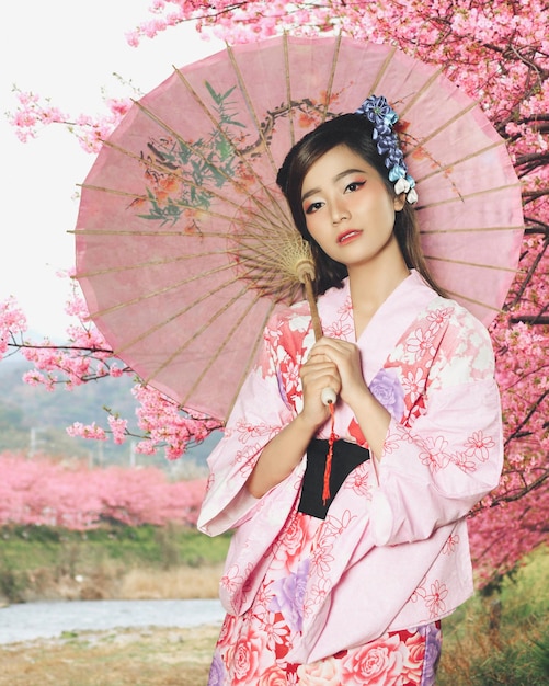 Retrato de una mujer joven con ropa tradicional y un paraguas de pie en el parque