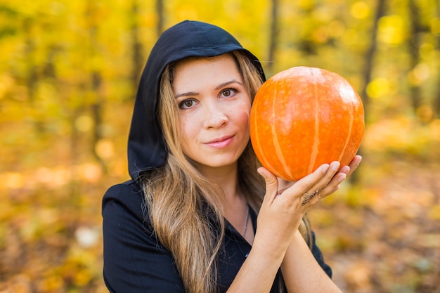 Retrato de la mujer joven rubia hermosa dramática que sostiene la calabaza en bosque. Día de Halloween.