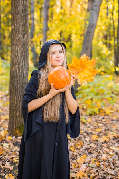 Retrato de la mujer joven rubia hermosa dramática que sostiene la calabaza en bosque. Día de Halloween.