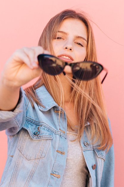 Retrato de una mujer joven rubia que sostiene las gafas de sol negras en la mano que mira la cámara