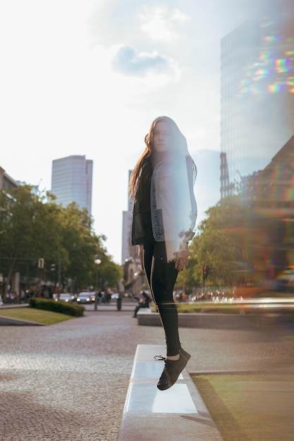 Retrato de una mujer joven saltando en un muro de contención contra el cielo en la ciudad