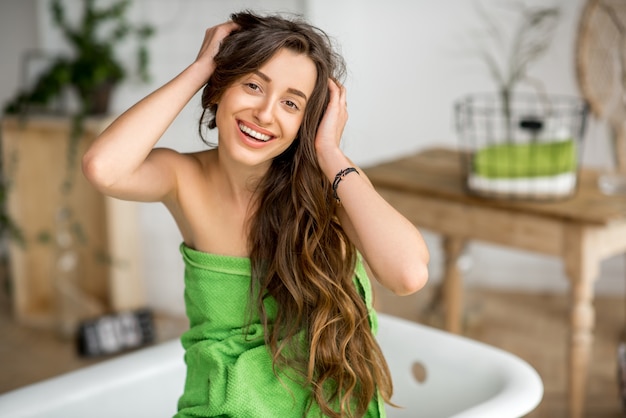 Foto retrato de una mujer joven sensible en una toalla verde sentada en el baño de lujo