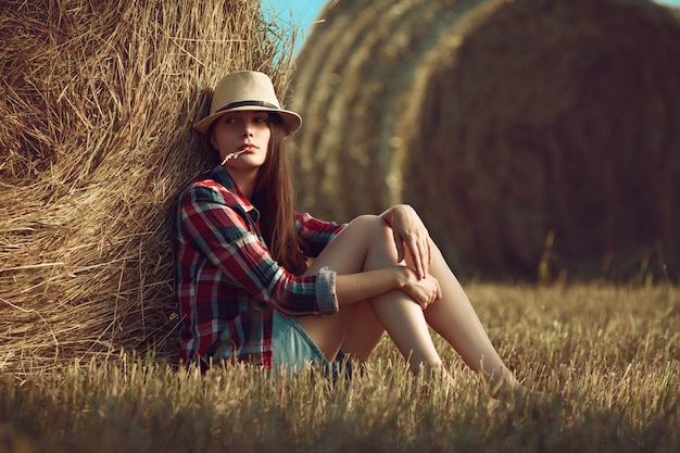 Retrato de mujer joven sentada junto a una pila de heno en la luz del sol