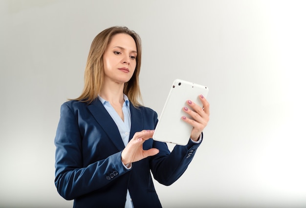 Retrato de mujer joven seria leyendo algo en su tableta blanca aislada en gris