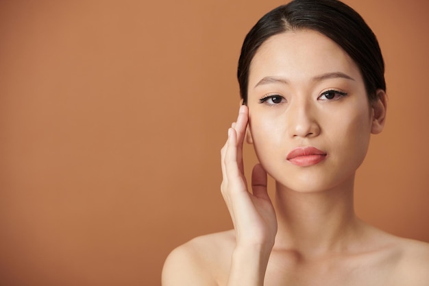 Retrato de mujer joven seria con maquillaje natural tocando la cara y mirando a la cámara