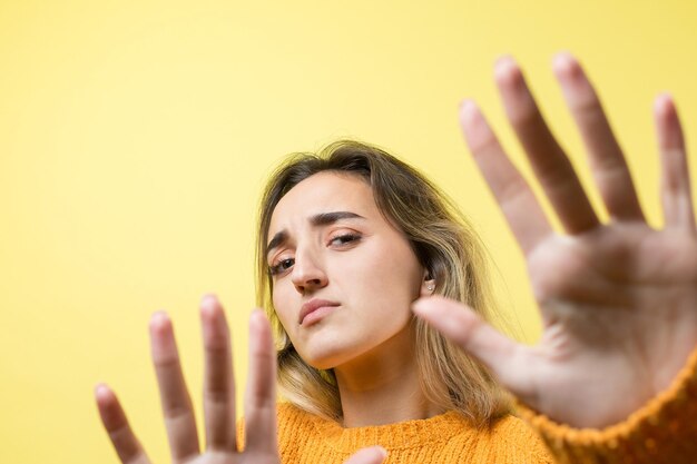 Retrato de una mujer joven seria mostrando gesto de parada con su palma sobre fondo amarillo