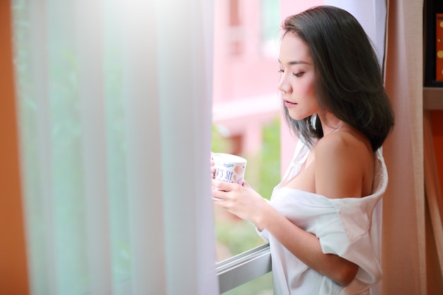 Retrato de mujer joven y sexy despierta y ve la vista desde la ventana del dormitorio