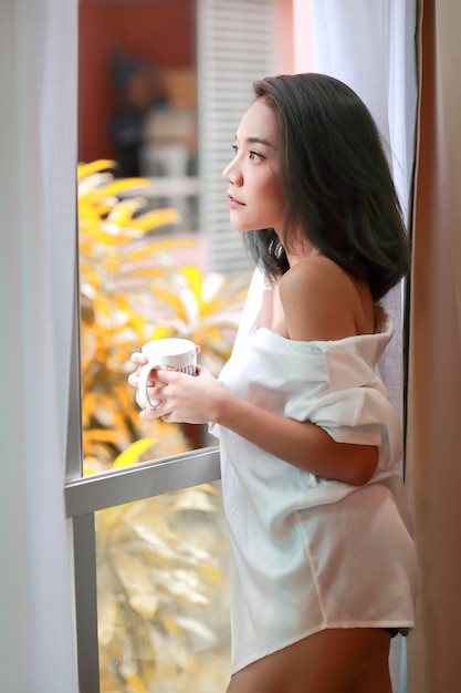 Retrato de mujer joven y sexy despierta y ve la vista desde la ventana del dormitorio