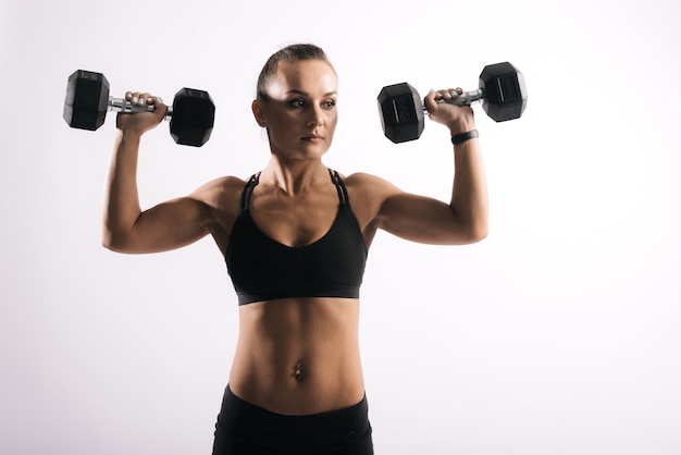 Retrato de mujer joven sexy muscular en ropa deportiva negra levantando pesas