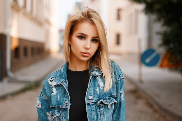 Retrato de una mujer joven sexy muy atractiva con maquillaje natural con ojos hermosos en una chaqueta de mezclilla de moda con un elegante vestido negro