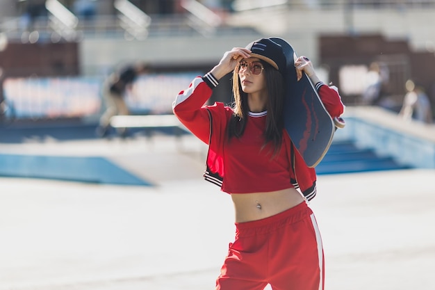 Retrato de mujer joven con sombrero negro ropa roja skater sosteniendo su patineta