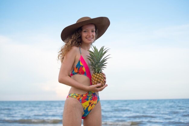 Retrato de una mujer joven con sombrero y con una piña contra el cielo