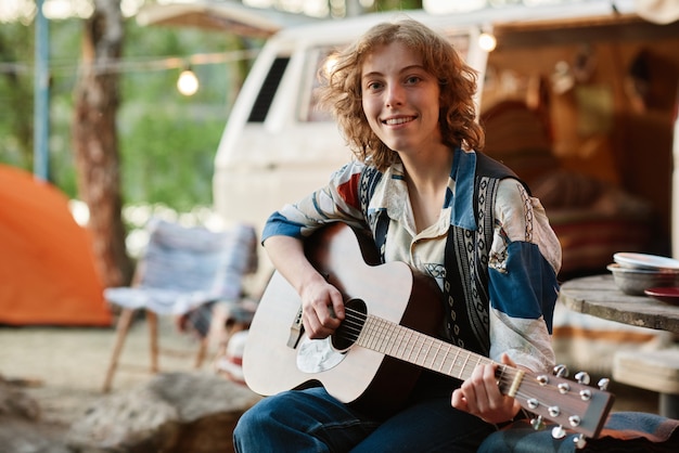 Retrato de mujer joven sonriendo a la cámara mientras toca la guitarra en la naturaleza