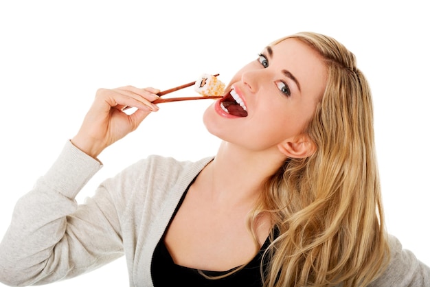 Retrato de una mujer joven sonriendo mientras come sushi contra un fondo blanco