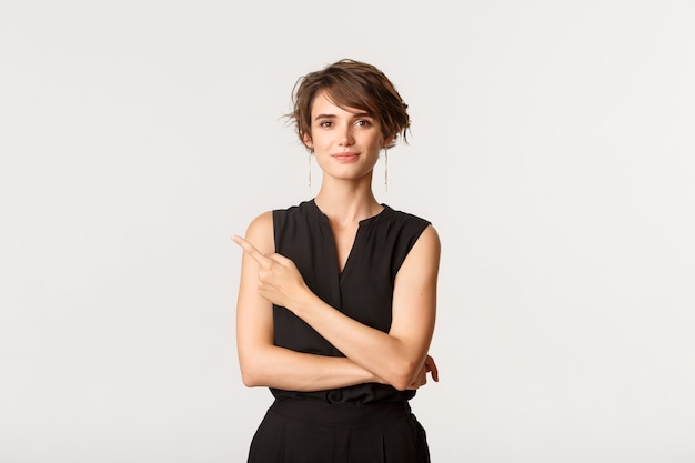 Retrato de mujer joven sonriente ambiciosa apuntando hacia la esquina superior izquierda y mostrando el banner, blanco.